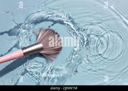 Makeup brush in clean water with a splash. Summer cosmetics concept. Top view. Stock Photo