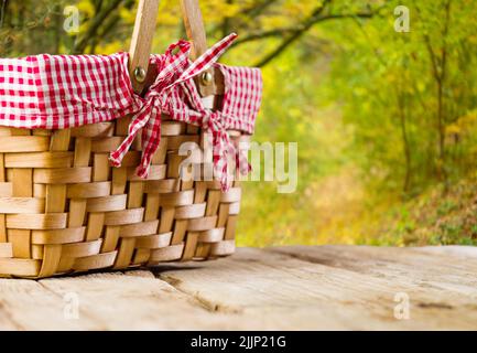 Against the background of picturesque autumn nature, a straw picnic basket on a simple wooden table. Country style. Close-up. The concept is rest, pic Stock Photo