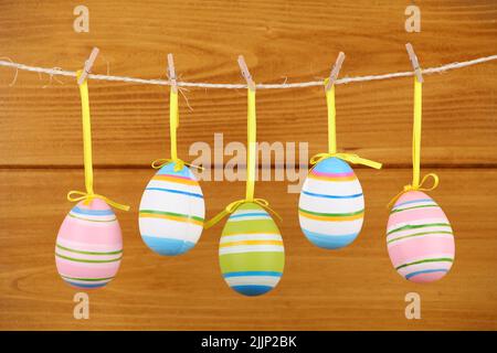Five colorful painted eggs hanging on a rope on a wooden background - Easter theme Stock Photo