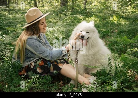 Young beautiful woman spending time with her white fluffy dog samoyed in the forest Stock Photo