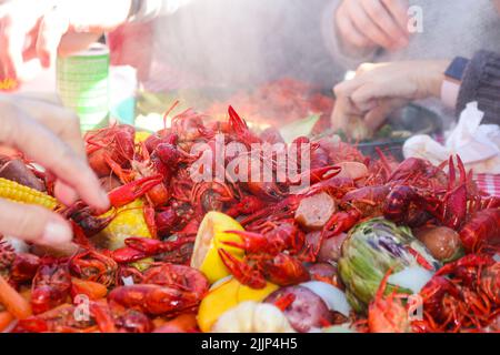 Steaming crayfish and lemons and sausages and artichokes and other vegestables piled on table with multiple hands reaching in to retreive food - selec Stock Photo