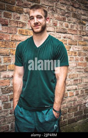 A vertical shot of a young Caucasian male standing against a brick wall Stock Photo