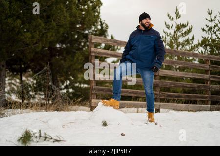A young caucasian man standing on the snow in the park during winter and laughing Stock Photo