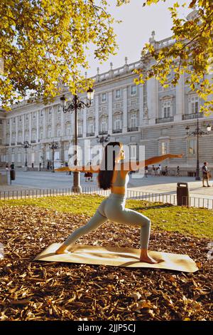 A Young Hispanic woman practicing yoga at sunset in front of the royal palace of Madrid, Spain Stock Photo