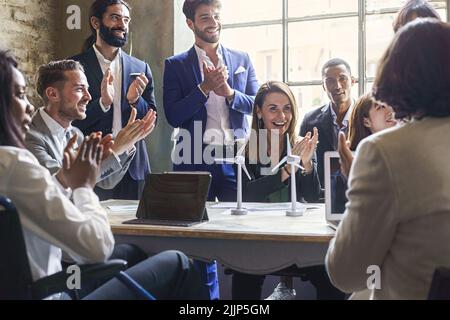 Group of multiethnic coworkers applauding the success of a sustainability project about renewable energy and green power - teamwork clapping hands sit Stock Photo