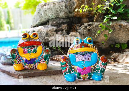 Two brightly colored and decorated ceramic frogs sit by landscaping rocks by swimming pool Stock Photo