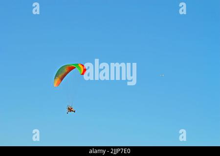 paramotor with para-glider pilot on blue sky, extreme sport diversity, motor hang glide aka tricycle with colorful sail Stock Photo