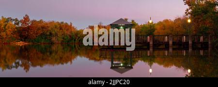 A panoramic view of a pier on a lake reflecting autumnal trees Stock Photo