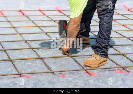 For a cement foundation, a construction worker twists steel bars with wire rod reinforcement using a rebar tying tool that is used to create rebar Stock Photo