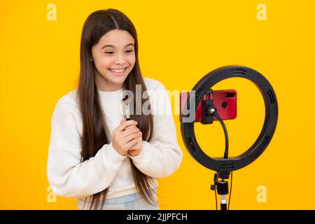 Beauty blog. Blogging, videoblog. Teenager child blogger with phone recording video on isolated yellow studio background. Influencer teen girl Stock Photo