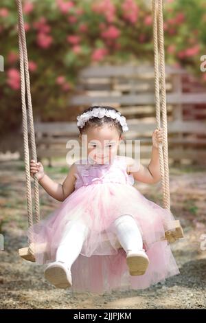 Smiling girl sitting on a swing in a garden, China Stock Photo