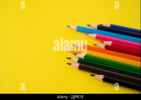 A row of unevenly arranged colored pencils on a yellow background with copy space. Stock Photo