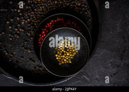Overhead view of bowls of pink, white and black peppercorns on a table Stock Photo