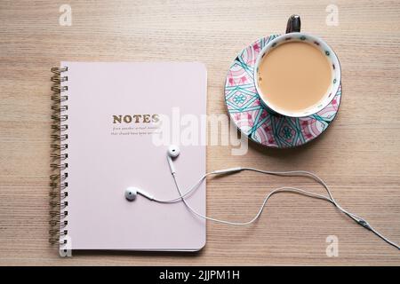 Notebook lying on the table with white headphones and a cup of tea in a teacup, pink, office supplies Stock Photo