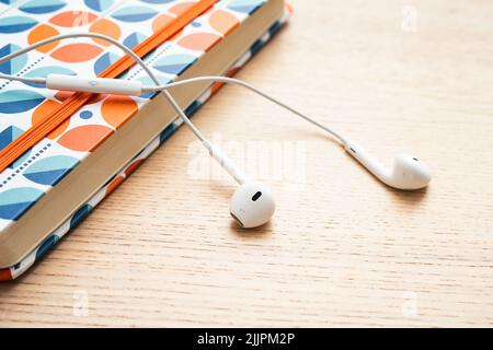 White headphones lying on the orange notebook Stock Photo