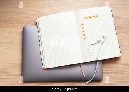 A top view of open notepad with 'to do list' text and headphones on laptop computer Stock Photo