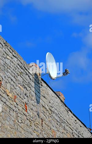 satellite dish antenna with convertors on the brick building wall on blue sky with white clouds, modern telecommunication diversity Stock Photo