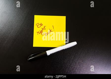 A 'be right back' text written in a yellow post-it note with pen on a table Stock Photo