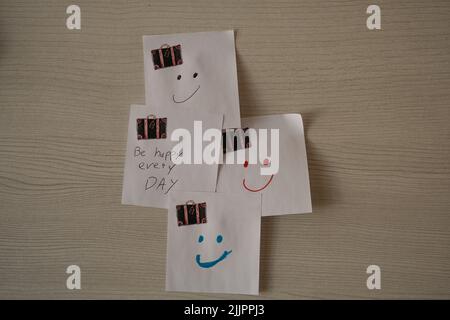 White sticky notes with smiley faces and a motivational quote on a wooden background Stock Photo