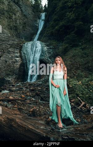 A beautiful view of a young woman with Romanian traditional clothes standing near a waterfall Stock Photo