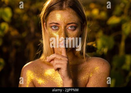 A closeup shot of a Caucasian female covered in gold glitter isolated on a blurred background Stock Photo