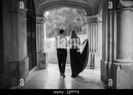 A greyscale back view of a couple walking in a hallway in evening outfit Stock Photo