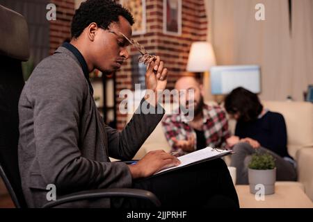 Stressed counselor taking notes on paper at couple therapy session with married partners, having relationship conflict and difficulties. Trying to solve problems with psychology advice. Stock Photo