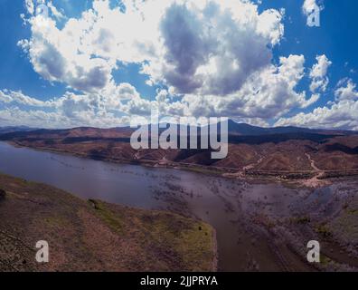 A wide-angle shot of a river in a rural area surrounded by mountains on a cloudy day Stock Photo