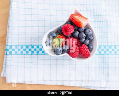 A top view of berries in a white bowl placed on a cloth Stock Photo