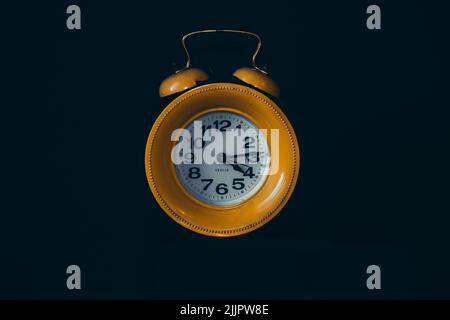 A classic yellow alarm clock isolated on a dark background Stock Photo