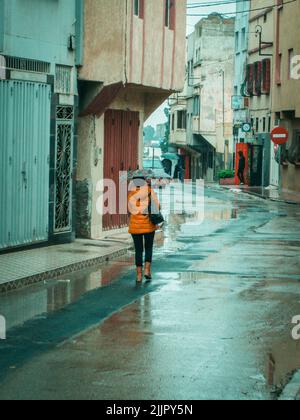 A female with a yellow jacket and umbrella walking in empty street on a rainy day Stock Photo