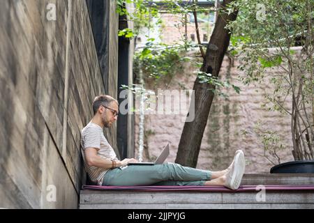 Young focused pensive European millennial guy freelancer working on laptop at outdoor workspace Stock Photo