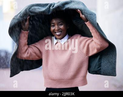 No umbrella, no problem. a young businesswoman using a jacket to cover with while going for a walk in the rain against an urban background. Stock Photo