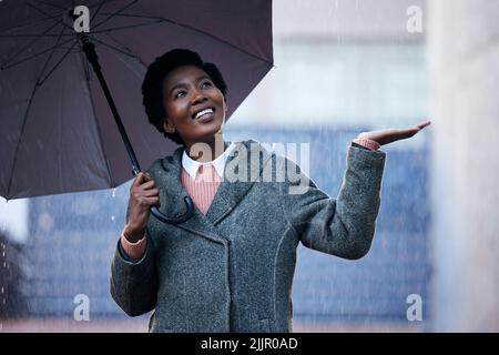 The rain wont stop me from moving forward. a young businesswoman using an umbrella to cover with while going for a walk in the rain against an urban Stock Photo