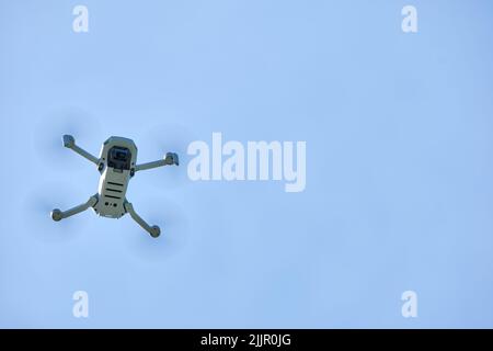 Ottawa, Ontario, Canada - May 23, 2022: A DJI Mavic Mini quadcopter drone is seen from below as it flies before a solid clear blue sky. Stock Photo