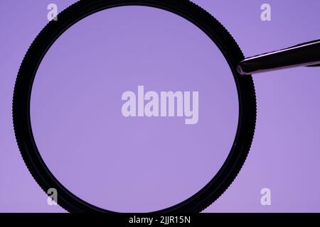 A closeup of a black magnifying glass on a light violet background Stock Photo