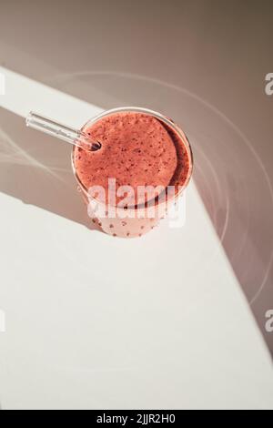 Pink mixed berry smoothie drink in polka dot glass with glass drinking straw on white table in sun Stock Photo