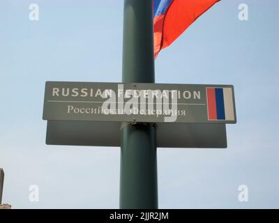 A sign with Russian Federation text on a flagpole with a waving flag against a blue sky Stock Photo