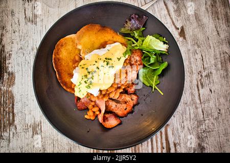 A top view of egg Benedict served with fried bread, bacon, and lettuce on a black plate Stock Photo