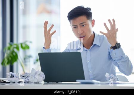 Frustrated, annoyed and irritated business man looking angry while working on his laptop. Young male worker feeling upset or struggling with an Stock Photo