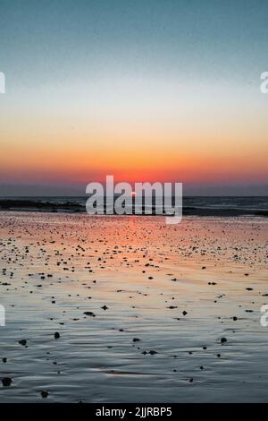A vertical of the sun setting and reflecting on the surface of the sea Stock Photo