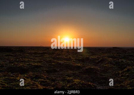 A scenic view of a mesmerizing sunset above the sea waves washing the shore Stock Photo
