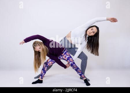 Young attractive yoga teacher and her little student doing performing intensive movements while exercising Stock Photo