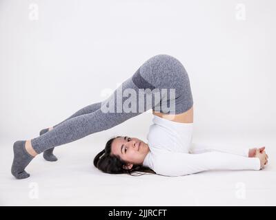 A young woman posing for yoga exercises on a light grey background Stock Photo