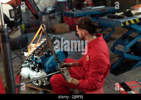 A young Caucasian car mechanic in a red uniform repairing the engine Stock Photo