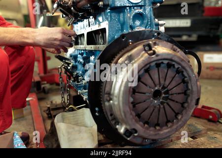 A young mechanic in a red uniform mounting the car engine Stock Photo