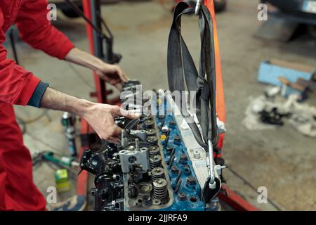 A young mechanic in a red uniform mounting the car engine Stock Photo