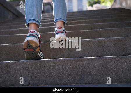 Woman wearing jeans and sneakers going up steep stairs Stock Photo