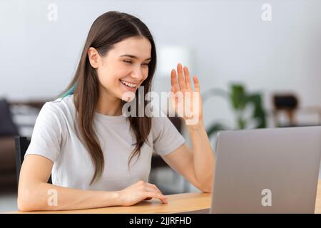 Smiling woman waving hand showing greeting gesture, looking at laptop screen Video call talking online concept Stock Photo