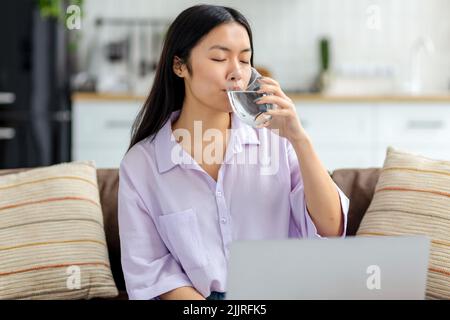 Portrait of young female freelancer drinking clean water sitting at workplace at home Stock Photo